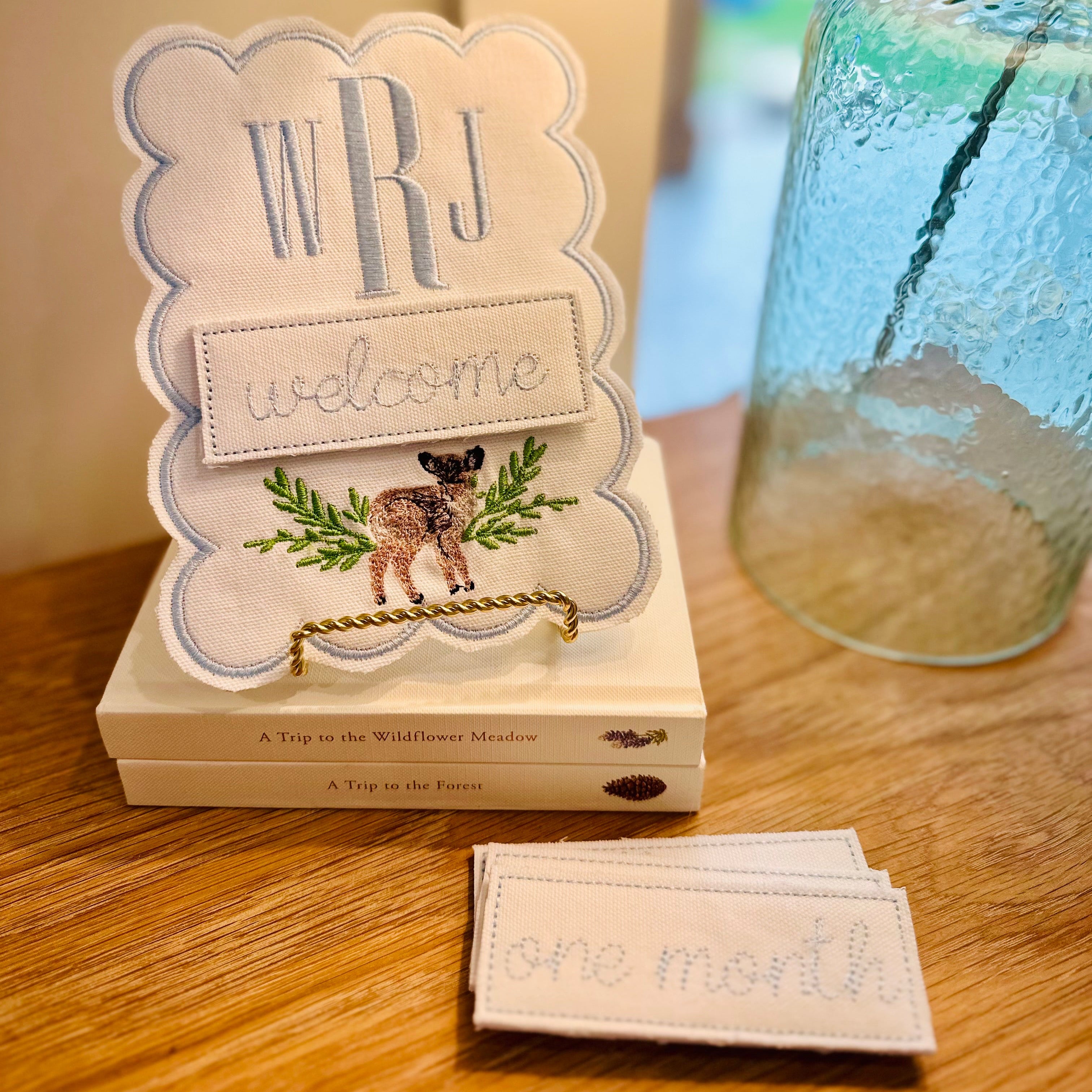 Decorative sign with 'WRJ Welcome' text on a wooden surface next to a glass jar.