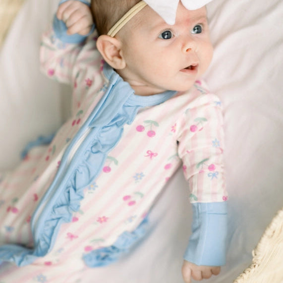 Baby in a crib wearing a onesie with pink stripes, cherries, and baby blue outline