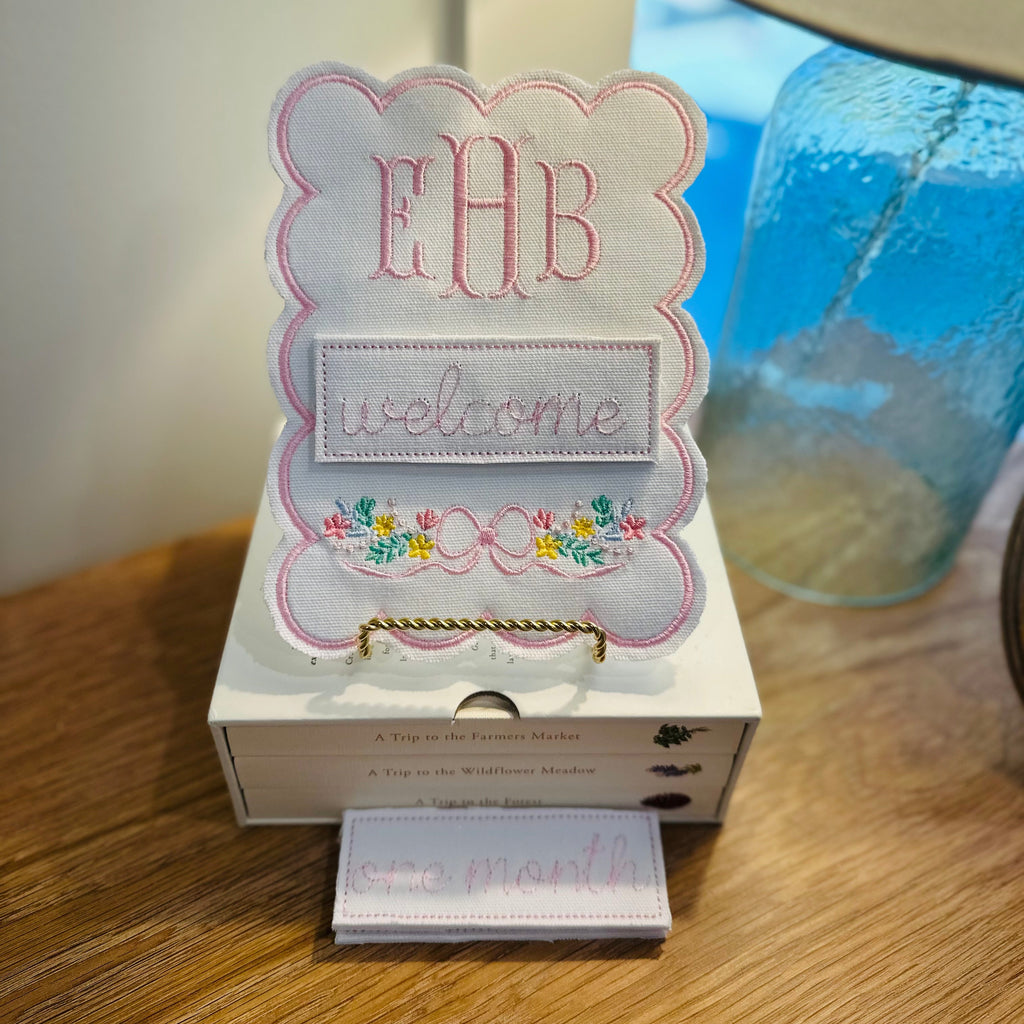 Decorative sign with 'EHB' and 'welcome' text on a wooden surface with a lamp in the background.