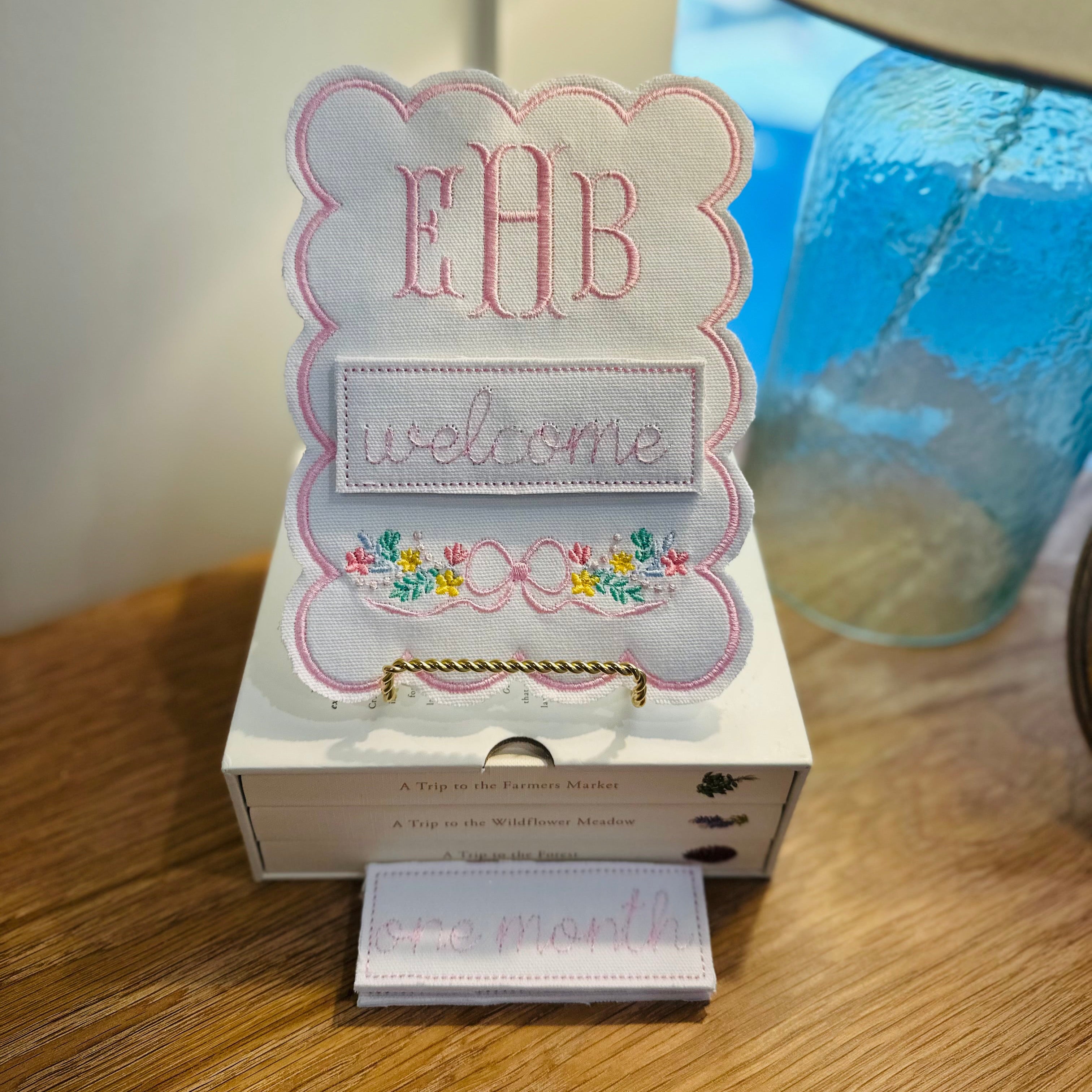 Decorative sign with 'EHB' and 'welcome' text on a wooden surface with a lamp in the background.