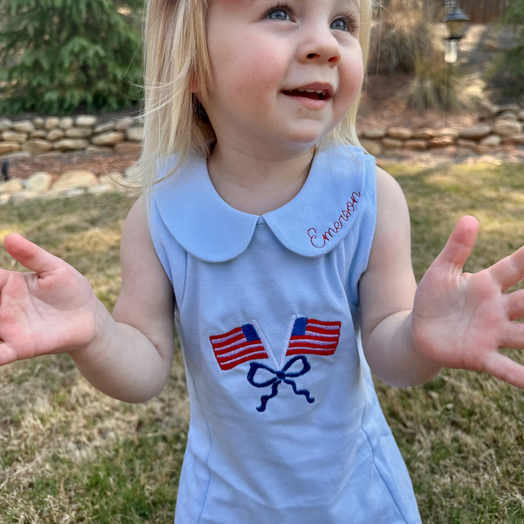 Child wearing a blue dress with American flag designs outdoors