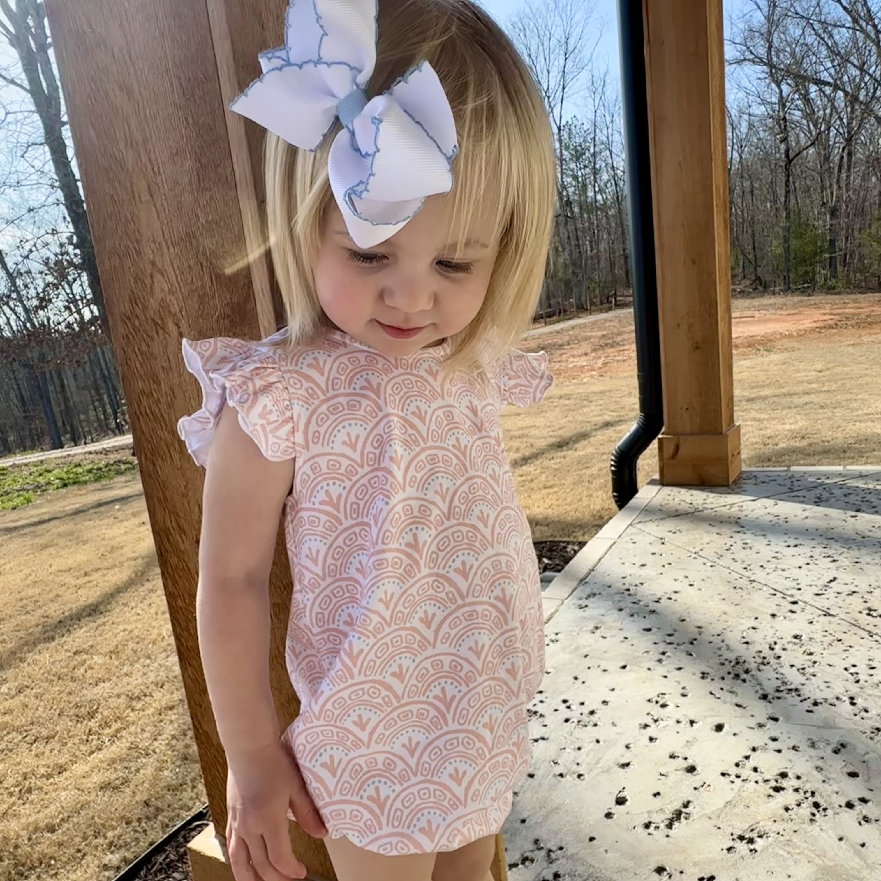 little girl in a white bubble romper with pink swirls and a white bow in hair